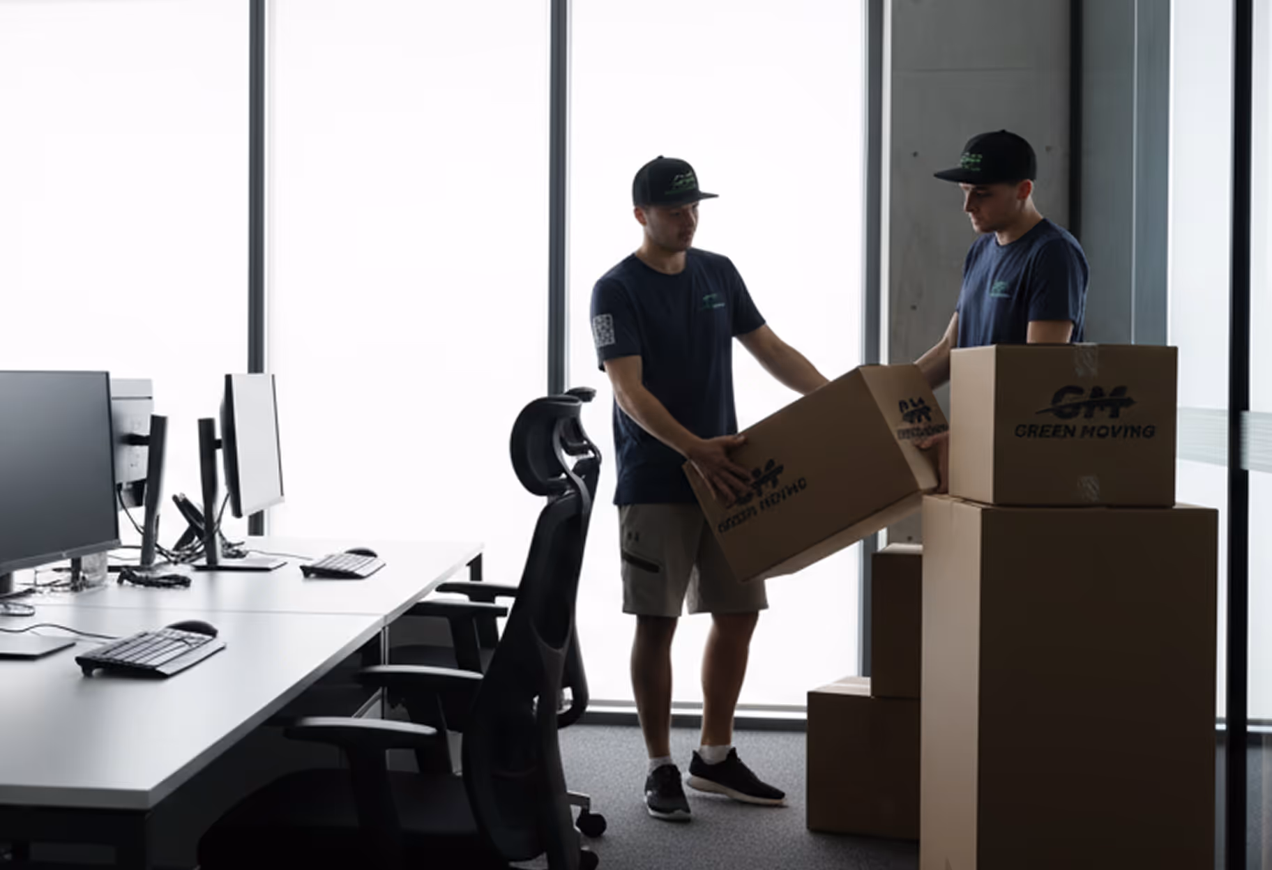 Movers stacking packed boxes beside office desks and computer monitors